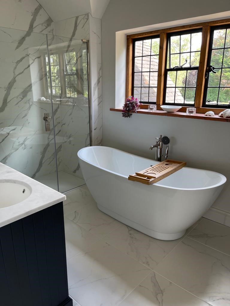 A marble-tiled en-suite with a freestanding slipper bath and walk-in shower, set beneath a leaded cottage window.