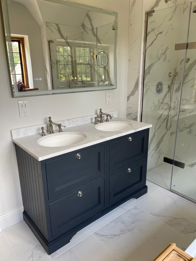 A navy double vanity with marble worktop and traditional brassware, alongside a marble walk-in shower.