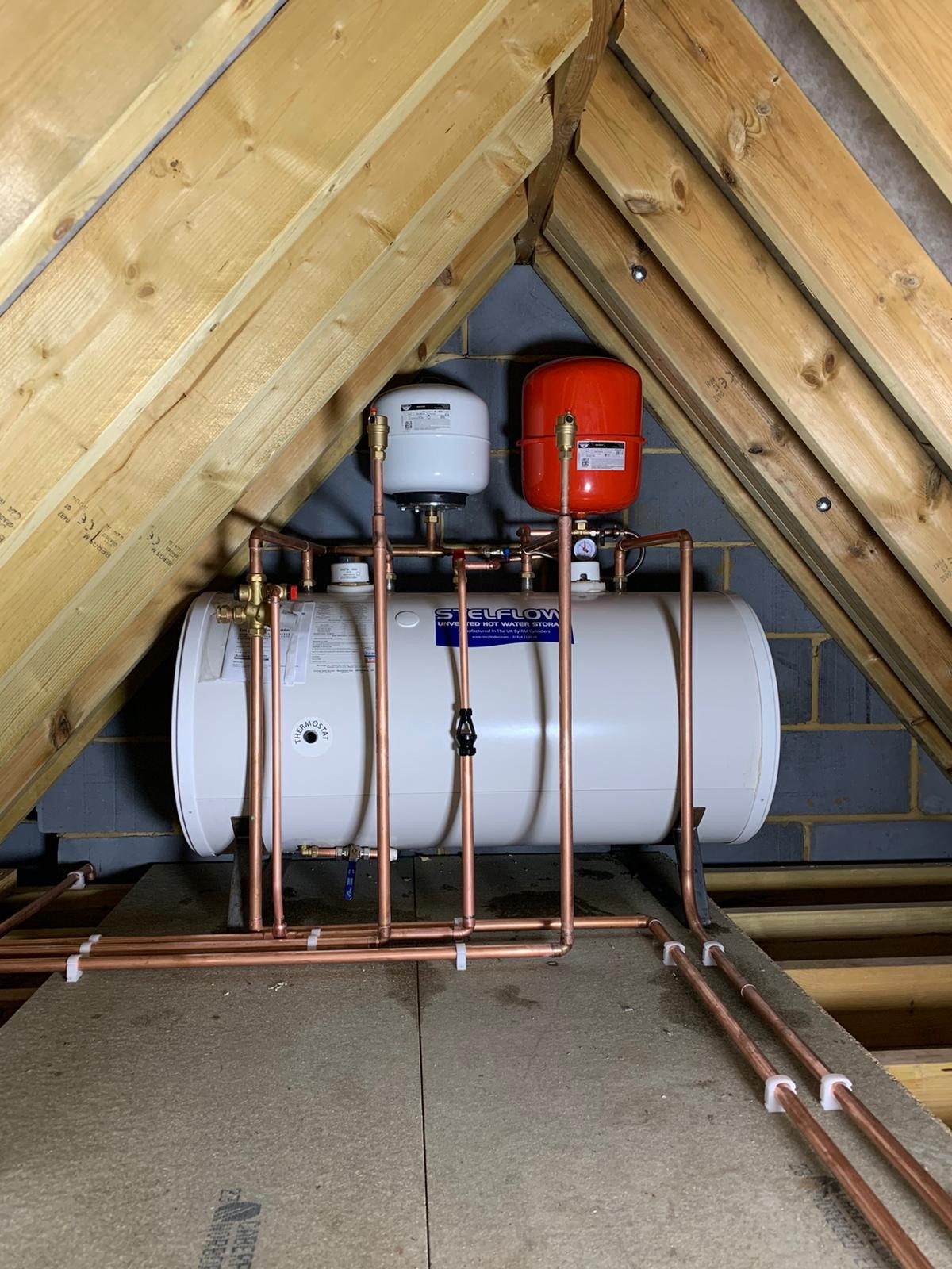 An unvented hot-water cylinder with expansion vessels and a red pressure-relief vessel, first-fixed in copper in the loft.